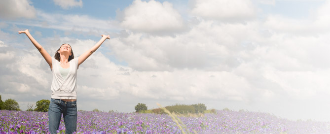 Woman throwing her hands up in a sunny field of purple flowers